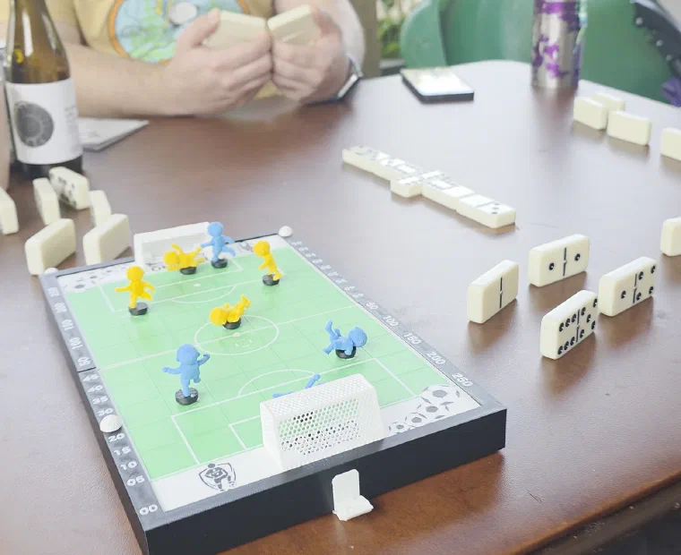Amigos jogando Domino Futebol Clube em casa com peças de dominó na mesa
